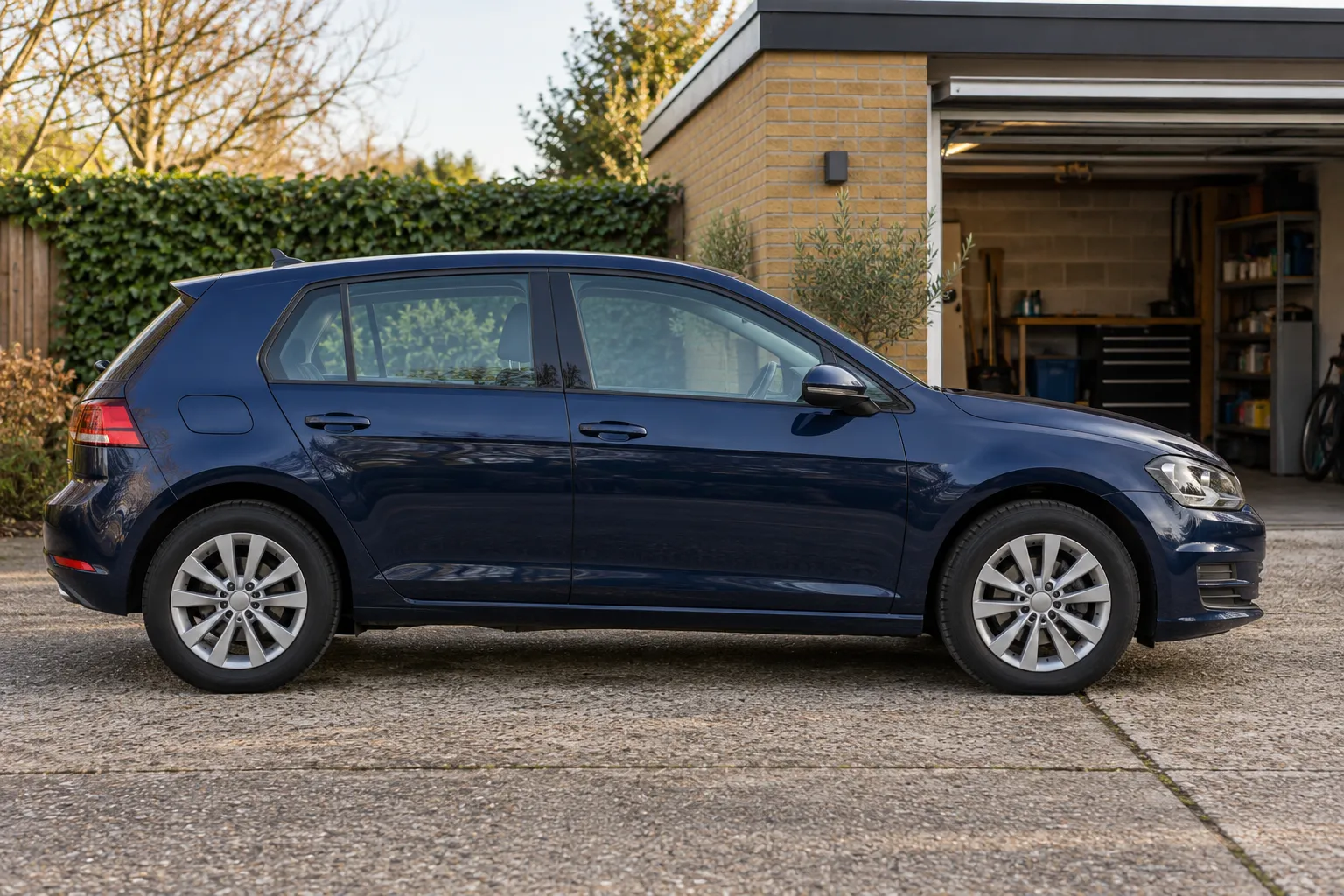 Donkerblauwe vijfdeurs hatchback geparkeerd voor een openstaande garage in ochtendlicht